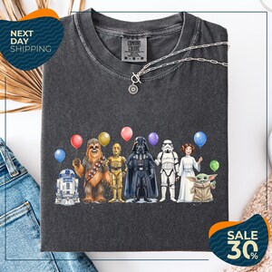 a black t-shirt with a graphic design of various characters from popular media, including Chewbacca, Darth Vader, Star Wars, and Baby Yoda, along with colorful balloons.
