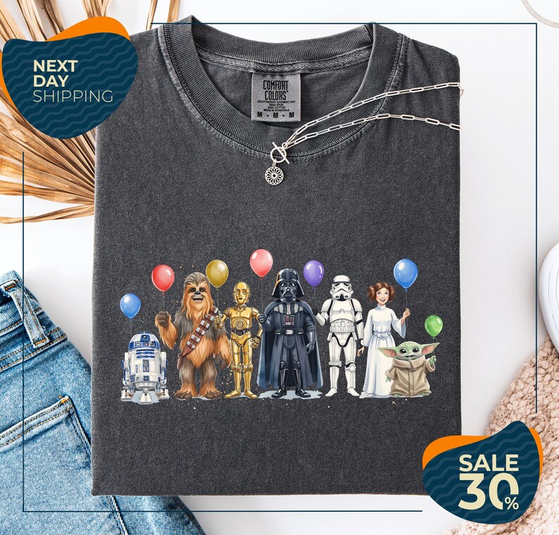 a black t-shirt with a graphic design of various characters from popular media, including Chewbacca, Darth Vader, Star Wars, and Baby Yoda, along with colorful balloons.