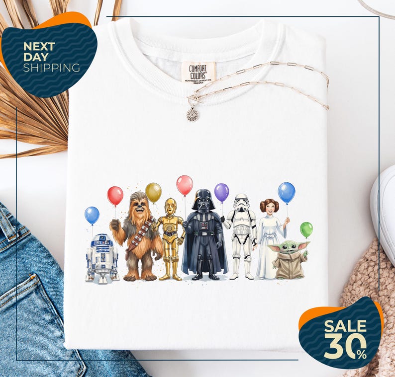 a white t-shirt with a graphic design of various characters from popular media, including Chewbacca, Darth Vader, Star Wars, and Baby Yoda, holding colorful balloons.