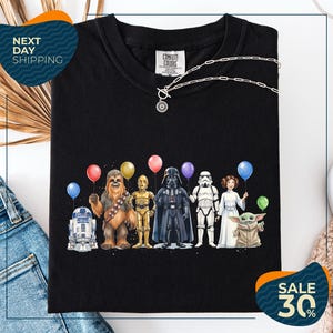 a black t-shirt with a graphic design of various characters from popular media, including Chewbacca, Star Wars, Darth Vader, and Baby Yoda, holding colorful balloons.