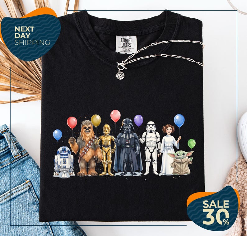 a black t-shirt with a graphic design of various characters from popular media, including Chewbacca, Star Wars, Darth Vader, and Baby Yoda, holding colorful balloons.