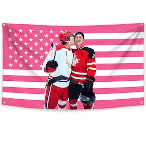 May include: A pink American flag with white stars and stripes forms the background for two hockey players. One wears a white and red jersey with the number 91, the other a red jersey with the number 2. Both are in hockey gear, embracing.