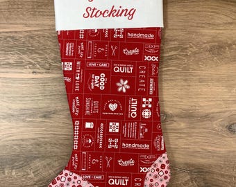 May include: A red Christmas stocking with a white cuff featuring the text My Stitchy Stocking in red script. The body has a grid pattern with white sewing-themed icons and text, while the toe and heel feature a pink fabric with red buttons.