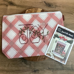 May include: A rectangular zippered project bag featuring a pink and white diamond plaid pattern with the word Joy embroidered in dark red cross-stitch with green accents, accompanied by a printed instruction card titled Joy to the World.