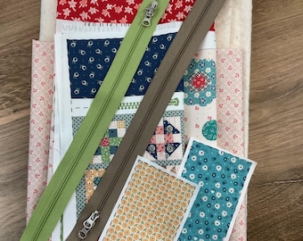 May include: A stack of assorted fabric pieces featuring floral and geometric patterns in red, blue, and white, topped with a light green zipper and a brown zipper, alongside two small rectangular fabric swatches with yellow and blue floral prints.