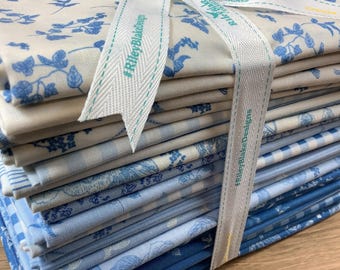 May include: A stack of folded fabric squares in various shades of blue and white, featuring floral, gingham, and striped patterns. The fabric bundle is tied with a white ribbon printed with the text #RileyBlakeDesigns and Riley Blake.