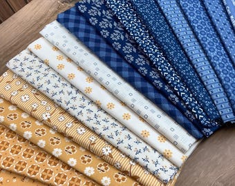 May include: A collection of folded fabric squares arranged in a fan shape, featuring a gradient from mustard yellow with floral and geometric patterns to deep blue with plaid, floral, and striped designs, including text on the edge.