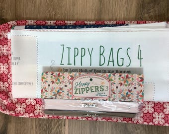 May include: A Zippy Bags 4 sewing pattern by Lori Holt of Bee in my Bonnet, featuring a white fabric panel with green text, placed atop a pink and white floral drawstring bag and a package of Happy Zippers 3, a set of 18-inch zippers.