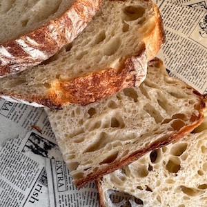 Peut inclure: Trois tranches de pain au levain avec une croûte dorée et croustillante et une mie aérée. Le pain présente une structure alvéolée distincte avec des poches d'air visibles dans le centre blanc, moelleux et tendre de chaque tranche.