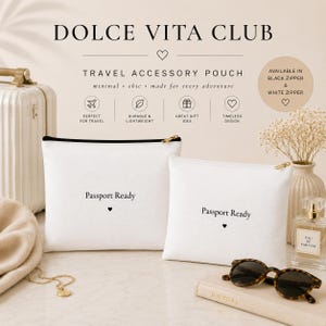 May include: Two white rectangular travel accessory pouches with black zips, each featuring the text Passport Ready and a small heart icon printed in black. The pouches are displayed alongside a suitcase, sunglasses, and a perfume bottle.