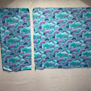 May include: Two pieces of fabric with a repeating pattern of stylized teal, purple, and blue cloud-like shapes. The fabric is displayed against a neutral, light-colored background.