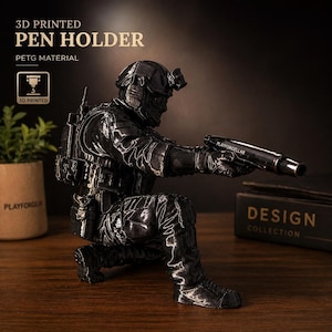 May include: A black 3D-printed pen holder shaped like a soldier in tactical gear, kneeling and aiming a pen. The pen holder has the text "PLAYFORGELLAB" on the pen. The words "3D PRINTED PEN HOLDER" and "PETG MATERIAL" are printed on the top.