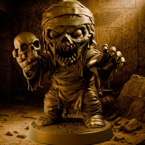 Puede incluir: Una figura dorada de una momia sosteniendo una calavera, ambientada en una tumba oscura. La momia tiene una expresión amenazante y está envuelta en vendas. El fondo incluye grabados jeroglíficos y un sarcófago de piedra, creando una atmósfera espeluznante.