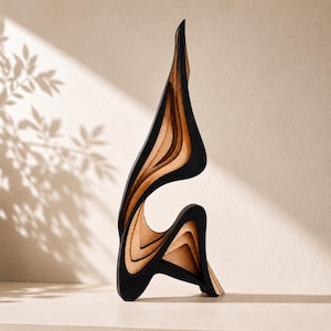 Peut inclure: Une sculpture abstraite verticale composée de panneaux de bois superposés. La pièce présente une alternance de sections en bois naturel clair et de bords noirs mats, créant une série de formes courbes fluides et d'espaces vides ouverts.
