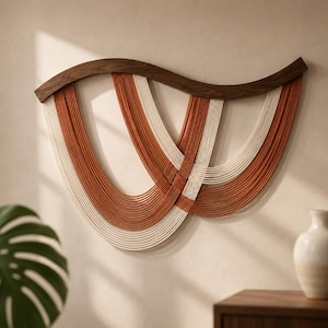 May include: A wall hanging featuring a curved dark brown wooden top piece with multiple strands of cream and terracotta colored cord draped in overlapping U-shaped patterns, creating a layered, symmetrical design across the horizontal frame.