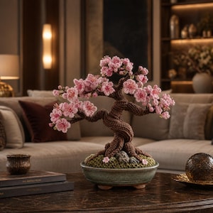 Op de afbeelding: Een handgemaakte bonsai boom met een bruine stam en delicate roze bloesems. De boom staat in een groene keramische pot, wat een miniatuurtuin-esthetiek creëert. De ingewikkelde details en zachte kleuren creëren een serene en artistieke woondecoratie.