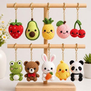 May include: A collection of handmade crochet keychains in various fruit and animal designs. The keychains include a red strawberry, green avocado, yellow pineapple, pink peach, red cherries, green frog, brown bear, white bunny, yellow chick, and a black and white panda.