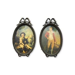 Puede incluir: Dos retratos antiguos enmarcados de forma ovalada. Uno representa a un joven con una oveja, el otro a una persona con una chaqueta roja y pantalones color canela. Los marcos son de metal oscuro con un lazo en la parte superior.