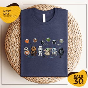 A blue t-shirt with a graphic design featuring various Star Wars characters, including Chewbacca, Stormtrooper, Baby Yoda, and Darth Vader, arranged in a row.
