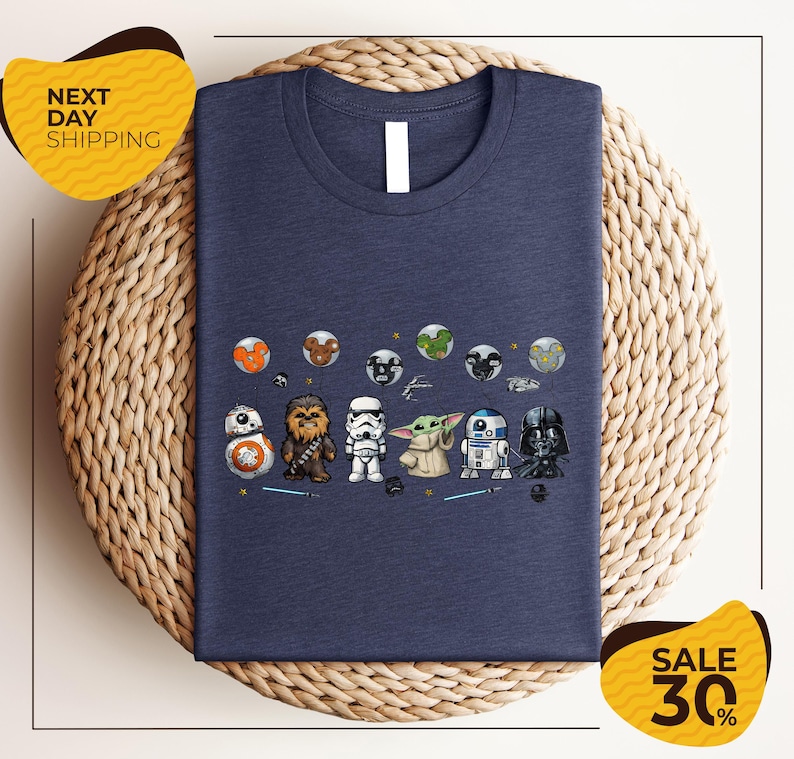 A blue t-shirt with a graphic design featuring various Star Wars characters, including Chewbacca, Stormtrooper, Baby Yoda, and Darth Vader, arranged in a row.