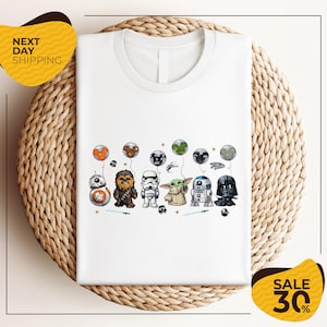 A white t-shirt with a graphic design featuring various Star Wars characters, including Chewbacca, Stormtrooper, Darth Vader, and Baby Yoda, along with other Star Wars-themed elements.