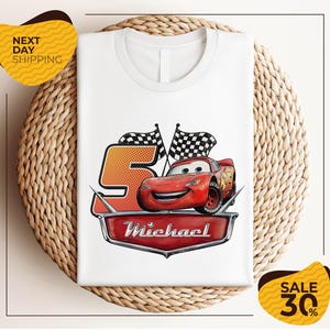 A white t-shirt with a graphic design featuring a red car and checkered flags, along with the text "Michael" and "Sale 30%".