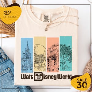 A white t-shirt with a graphic design featuring illustrations of various Disney landmarks, including the Eiffel Tower, the castle, and the roller coaster, along with the text "Walt Disney World". The t-shirt is displayed on a white background, and there are yellow and black sale signs indicating a 30% discount.