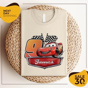 A t-shirt with a design featuring a red car and checkered flags, along with the text "James" and the number "9". The t-shirt is displayed on a woven basket, and there are yellow price tags with text indicating a sale of 30% off.