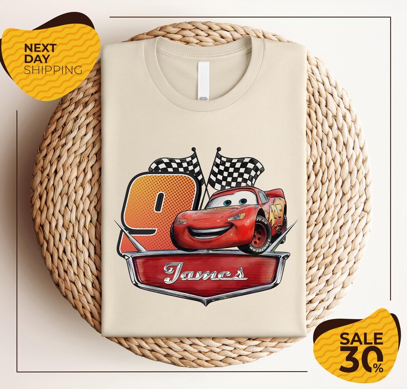 A t-shirt with a design featuring a red car and checkered flags, along with the text "James" and the number "9". The t-shirt is displayed on a woven basket, and there are yellow price tags with text indicating a sale of 30% off.