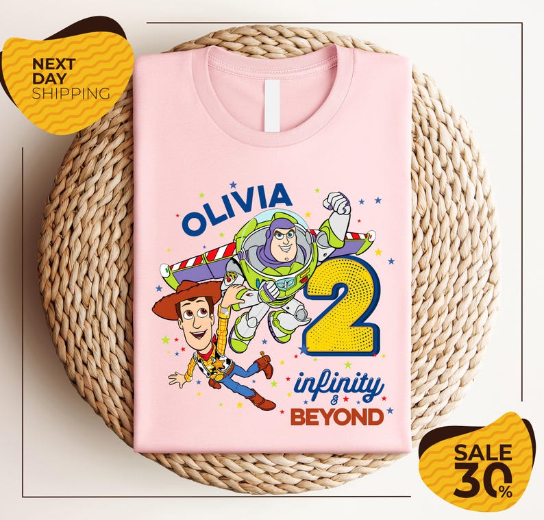A pink t-shirt with a cartoon image of Buzz Lightyear and Woody from Toy Story, along with the text "Olivia 2 Infinity Beyond". The t-shirt is displayed on a woven basket, and there are yellow price tags with text indicating a sale of 30% off.