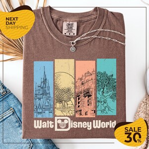 a brown t-shirt with a graphic design of Disney World landmarks, including a castle, roller coaster, and other iconic structures. The t-shirt is displayed on a white background, and there are two yellow sale signs indicating a 30% discount on the item.