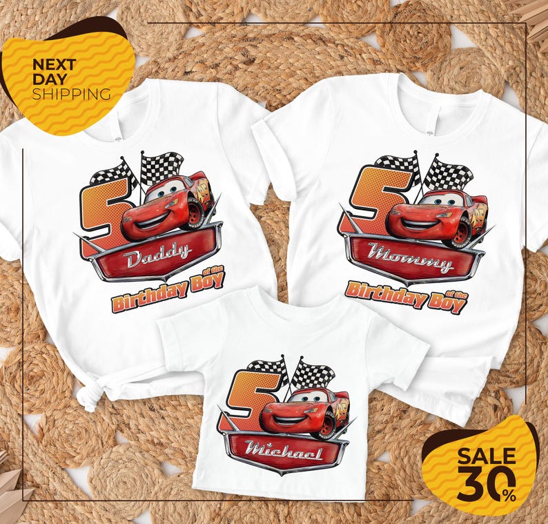 a collection of white t-shirts featuring the character Lightning McQueen from the Cars movie, along with the text "Daddy Birthday Boy" and "Michael Birthday Boy". The t-shirts are arranged on a textured background, and there is a yellow banner with the text "NEXT DAY SHIPPING" and a sale offer of "SALE 30%".