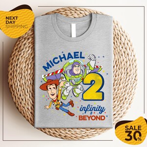 A gray t-shirt with a graphic design featuring characters from the Toy Story franchise, including Buzz Lightyear and Woody, along with the text "Michael 2 Infinity & Beyond".