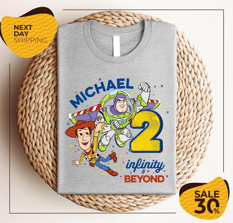 A gray t-shirt with a graphic design featuring characters from the Toy Story franchise, including Buzz Lightyear and Woody, along with the text "Michael 2 Infinity & Beyond".
