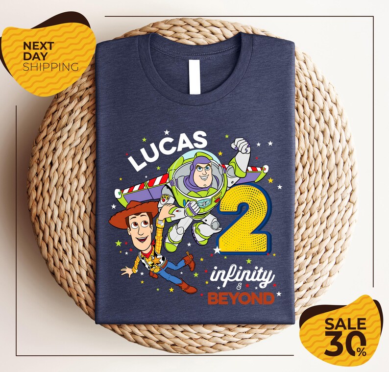 A blue t-shirt with a graphic design featuring Buzz Lightyear and Woody from Toy Story, along with the text "Lucas 2" and " Infinity & Beyond".
