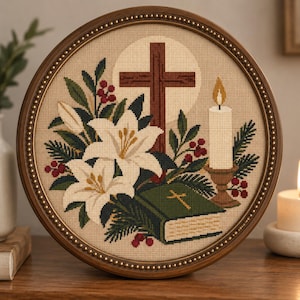 May include: A circular framed cross-stitch embroidery featuring a brown wooden cross, white lilies, green pine branches, red berries, a lit candle in a holder, and a green book with a gold cross on the cover, all set against a beige fabric background.