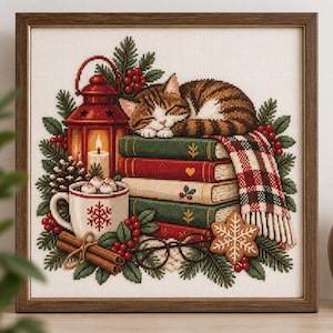 May include: A cross-stitch embroidery in a brown frame depicting a tabby cat sleeping on a stack of books. The scene includes a red lantern, a mug of hot cocoa with marshmallows, cinnamon sticks, a plaid blanket, pine branches, and berries.