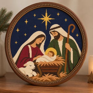 Puede incluir: Un bordado en punto de cruz con marco circular que representa una escena de natividad con una estrella central sobre un cielo azul oscuro. La imagen muestra figuras con túnicas, un bebé en un pesebre y un pequeño cordero blanco.