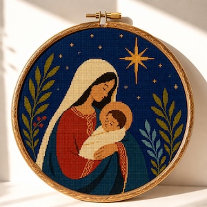 Könnte beinhalten: Ein runder Stickrahmen mit einem Kreuzstichmotiv, das eine Figur mit weißem Kopftuch und rotem Gewand zeigt, die ein eingewickeltes Baby hält. Der Hintergrund ist dunkelblau mit einem gelben Stern und grünen Blattzweigen an den Seiten.