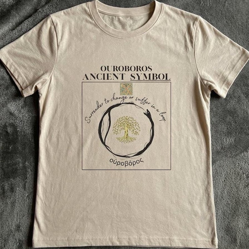 May include: A beige t-shirt featuring the text "OUROBOROS ANCIENT SYMBOL" above a circular design with a tree and the Greek word "&omicron;&upsilon;&rho;&omicron;&beta;ό&rho;&omicron;&sigmaf;". The design includes the phrase "Surrender to change or suffer in a loop."
