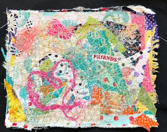 May include: A colorful textile art piece with a patchwork design. The artwork features a heart shape, the word "Friends", and the word "Happy". The piece is made of various fabrics in shades of pink, green, orange, and yellow.