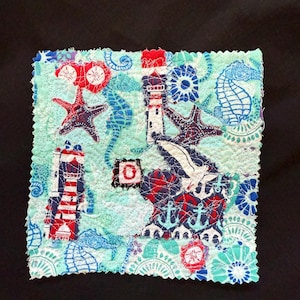May include: A colorful fabric patchwork with a nautical theme. The patchwork features lighthouses, seahorses, anchors, and starfish in shades of red, blue, and white on a light blue background.