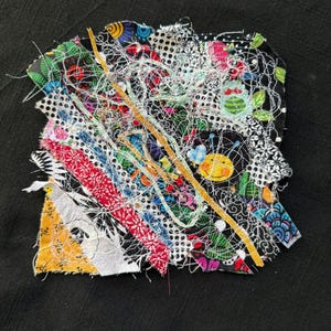 May include: A colorful textile art piece with layered fabric strips and intricate stitching. The design features floral patterns, a yellow bee, and a mix of red, white, and blue hues, set against a black background.