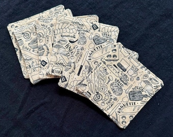 May include: Set of six beige fabric coasters with a black and white pattern of various bread-making items, including loaves of bread, baguettes, flour, and a whisk. The text "BAGUETTE" is printed on the coasters.