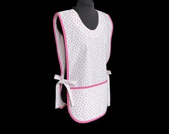 May include: A white apron with a pink floral pattern and pink trim. The apron has a pocket and ties at the waist. The apron is displayed on a black mannequin.