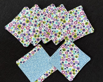 May include: Set of eight floral print fabric coasters. The coasters are square and feature a white background with pink, green, and blue flowers. Two of the coasters have a blue fabric border.