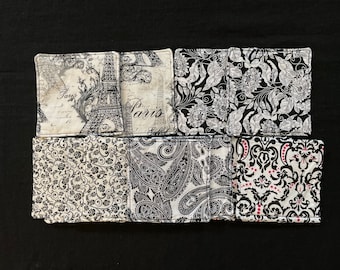 May include: Six black and white fabric coasters with different patterns. The coasters feature floral, paisley, and damask designs. Two of the coasters have the word "Paris" printed on them.