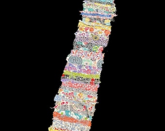 May include: A long strip of fabric made from many different colorful patterned pieces of fabric sewn together. The fabric is arranged vertically and has a variety of floral, geometric, and abstract patterns.