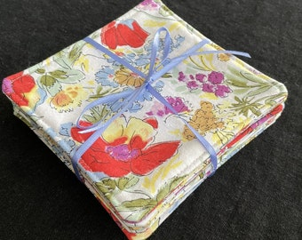 May include: A stack of four floral fabric coasters tied together with a blue ribbon. The coasters feature a white background with a colorful floral pattern.