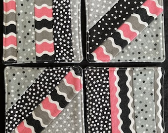 May include: Set of four square fabric coasters with a patchwork design. The coasters feature black, white, gray, and pink fabric with polka dots, wavy lines, and diagonal stripes.